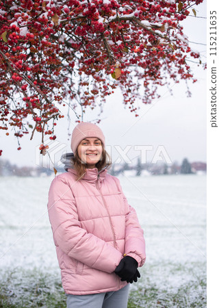 Winter Elegance: Portrait of a Beautiful Girl in a Snowy European Village. Winter lifestyle portrait of cheerful pretty girl. Smiling and having fun in the snow park. Snowflakes falling down 115211635