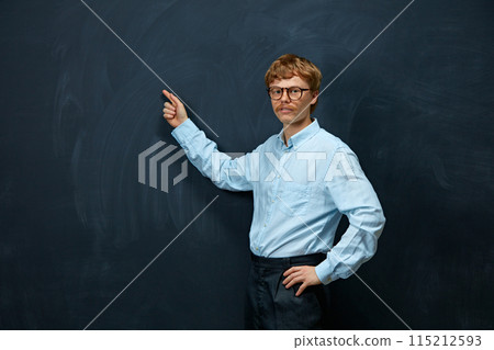 Portrait of young man, teacher or tutor in formal attire pointing standing against writing board background, and looking at camera Portrait of young man, teacher or tutor in formal attire pointing standing against writing board background, and looking at camera 115212593
