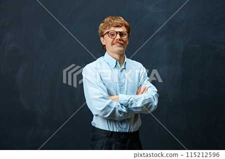 Young man wearing formal attire looking confident at camera and crossed hands on breast against writing board background. Young man wearing formal attire looking confident at camera and crossed hands on breast against writing board background. 115212596
