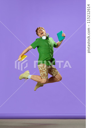 Young guy dressed casual summer attire jumping of joy and happiness holding books against purple background. Young guy dressed casual summer attire jumping of joy and happiness holding books against purple background. 115212614