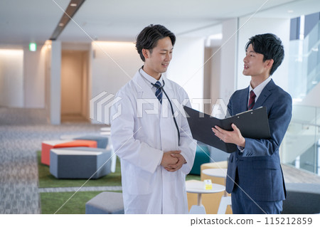 Smiling male doctor and medical representative having a conversation at the hospital 115212859