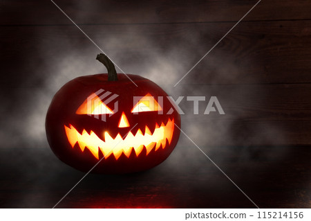 pooky Halloween pumpkin, Jack O Lantern, with an evil face and eyes on a wooden table with a misty gray background. 115214156
