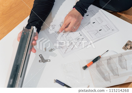 Hands of a woman assembling a metal piece of furniture following instructions 115214268