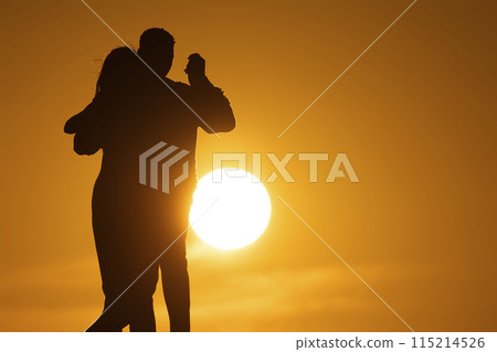 A couple is dancing in the sun, with the sun in the background A couple is dancing in the sun, with the sun in the background 115214526