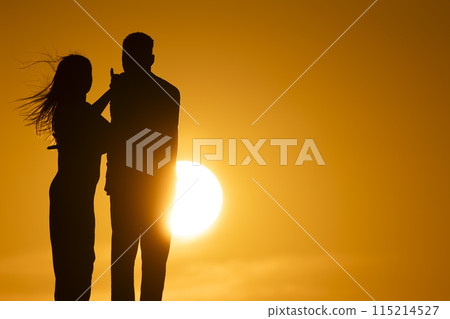 A couple standing in front of a sun with the woman touching the man's arm A couple standing in front of a sun with the woman touching the man's arm 115214527