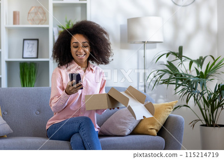 Smiling woman sitting on a couch with a smartphone and opened parcel, delightedly writing a review of her online shopping experience. Smiling woman sitting on a couch with a smartphone and opened parcel, delightedly writing a review of her online shopping experience. 115214719