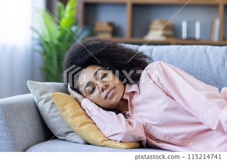 Young woman sleeping peacefully on a couch in a cozy home living room setting, showcasing relaxation and comfort. Young woman sleeping peacefully on a couch in a cozy home living room setting, showcasing relaxation and comfort. 115214741