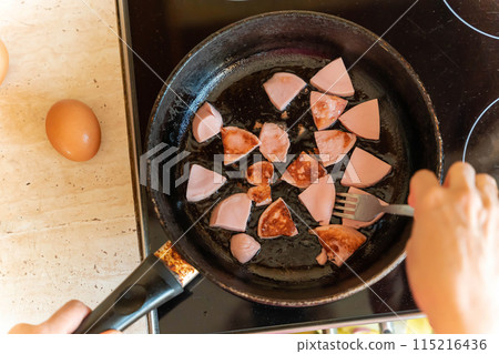 Close-up overhead view of sausage slices frying in a pan on the stove 115216436