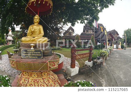 The outdoor golden Buddha statue under the trees inside Wat Nantaram temple is beautiful with Thai Yai art. Features an entire teak temple decorated with beautifully carved wood. Located in Thailand. The outdoor golden Buddha statue under the trees inside Wat Nantaram temple is beautiful with Thai Yai art. Features an entire teak temple decorated with beautifully carved wood. Located in Thailand. 115217085