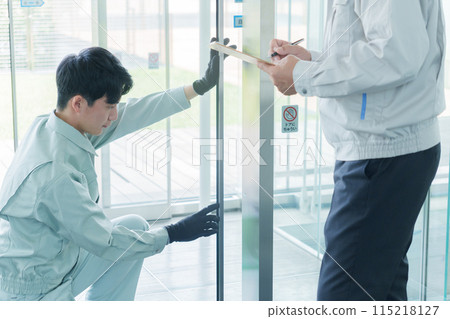 Worker performing maintenance on automatic doors 115218127