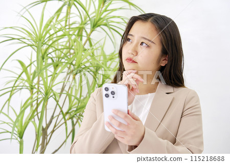 年輕女商人在辦公室思考時使用智慧型手機 115218688
