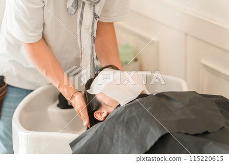 A woman shampooing at a shampoo table in a beauty salon and a hairdresser/stylist A woman shampooing at a shampoo table in a beauty salon and a hairdresser/stylist 115220615