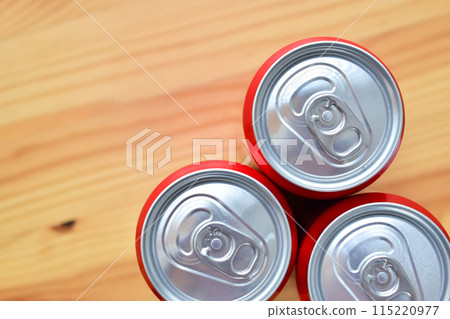 three aluminium red cans of soft drink put on brown wooden table 115220977