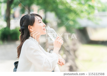 A smiling businesswoman hydrates and refreshes herself by the river A smiling businesswoman hydrates and refreshes herself by the river 115222508