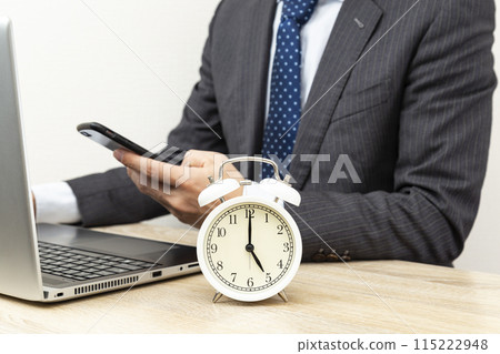 A man in a suit sitting in front of a computer and a clock on a white background A man in a suit sitting in front of a computer and a clock on a white background 115222948