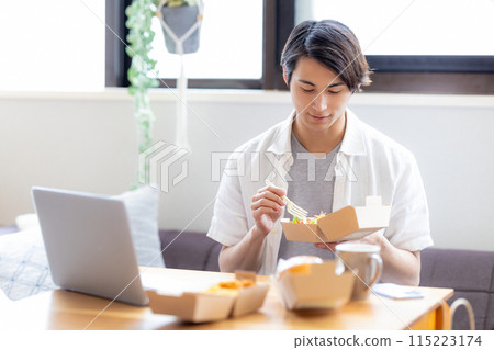 一名男子一邊看著電腦，一邊吃著外帶訂購的食物 115223174