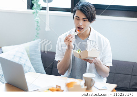 一名男子一邊看著電腦，一邊吃著外帶訂購的食物 115223175