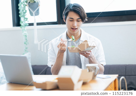 一名男子一邊看著電腦，一邊吃著外帶訂購的食物 115223176