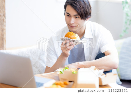 一名男子一邊看著電腦，一邊吃著外帶訂購的食物 115223351