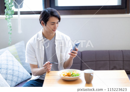 A man eating while looking at his smartphone 115223623