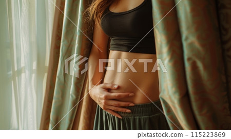 Natural beauty, an unretouched, cropped portrait of a woman by a window, showcasing her exposed midriff 115223869