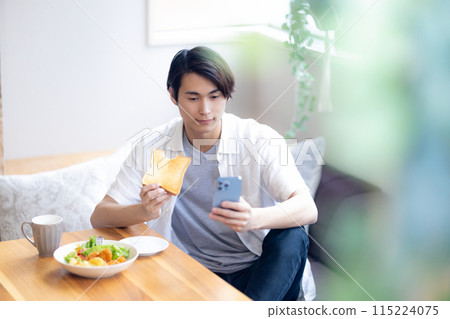 一名男子邊吃邊看智慧型手機 115224075