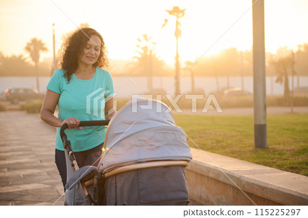 Happy smiling mother walking with baby in pram outdoors on the nature at sunset Happy smiling mother walking with baby in pram outdoors on the nature at sunset 115225297