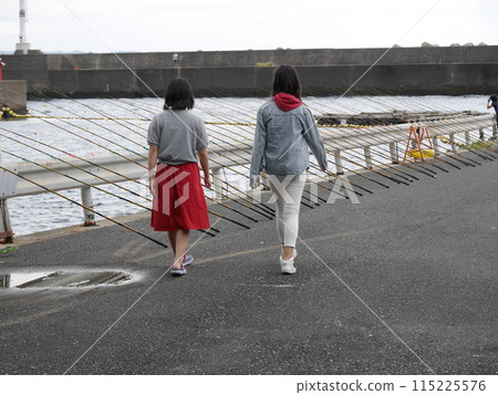 Two sisters walking along a harbor lined with fishing rods 115225576