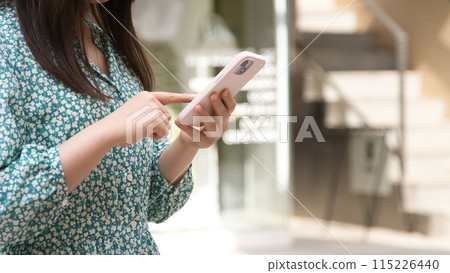 A young woman operating a smartphone on a street corner 115226440