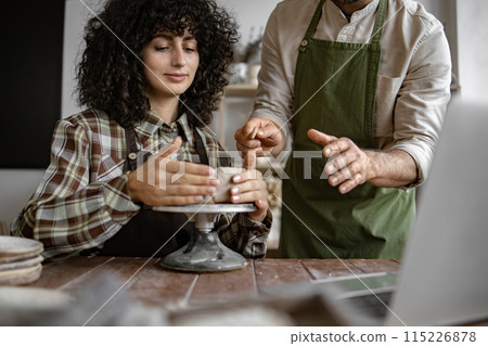 Man teaching woman pottery in creative studio setting 115226878