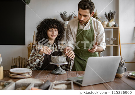 Male pottery instructor teaching female student in studio with laptop Male pottery instructor teaching female student in studio with laptop 115226900