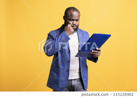 African american man browsing though financial report pages, isolated over studio background. Worker reading clipboard with files containing economic graphs and figures, solving business tasks African american man browsing though financial report pages, isolated over studio background. Worker reading clipboard with files containing economic graphs and figures, solving business tasks 115226902