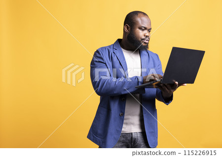 Man looking at business diagram and figures on laptop, isolated over studio background. BIPOC employee checking company financial annual report charts on notebook screen 115226915