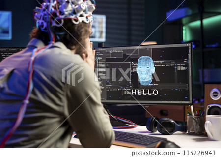 IT professional using EEG headset to communicate with artificial intelligence on computer in binary code. Software developer sending brainwave signals to AI entity on PC using high tech device IT professional using EEG headset to communicate with artificial intelligence on computer in binary code. Software developer sending brainwave signals to AI entity on PC using high tech device 115226941