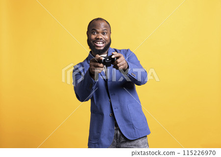 Cheerful player happy after winning gaming console game, isolated over studio background. Joyful man satisfied after being victorious in videogame, defeating all enemies using gamepad 115226970