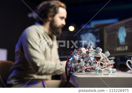 Focus on EEG headset used by engineer in blurry background to upload consciousness into computer. Close up shot of high tech gear used by IT expert to create connection between brain and PC 115226975