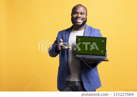 Happy african american man holding green screen laptop, doing endorsement. Cheerful BIPOC person presenting mockup notebook, doing positive evaluation, isolated over studio background 115227004
