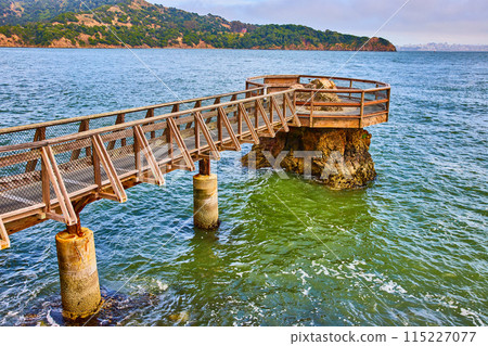 Choppy water around Elephant Rock pier with clear coastline and distant city across bay 115227077