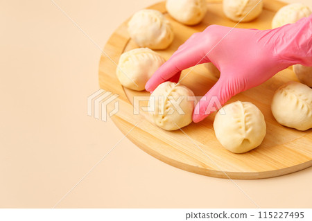 Close-up of skilled chef's hand in rubber glove arranging traditional Central Asian manty with meat on wooden board, frozen semi-finished products, copy space. 115227495