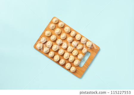 Top view of a wooden board with neatly laid out semi-cooked dumplings on blue background. 115227553