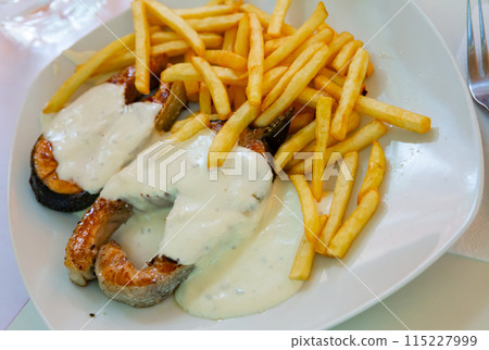 Tasty fried salmon with white sauce and french fries potatoes on plate 115227999