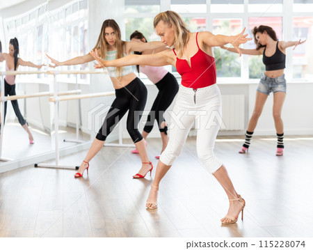 During lesson, woman learn to move and perform dance in heels with women companions During lesson, woman learn to move and perform dance in heels with women companions 115228074