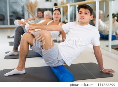 Young man practicing pilates with blue roller in gym room Young man practicing pilates with blue roller in gym room 115228299