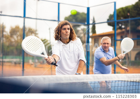 Concentrated man playing padel tennis on open court Concentrated man playing padel tennis on open court 115228303