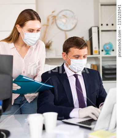 Businessman in face mask working with female assistant in office Businessman in face mask working with female assistant in office 115228341