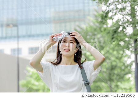 A woman wiping sweat from her forehead with a handkerchief and worrying about the sun 115229500