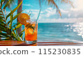 cold cocktail in glass with straw and ice on the table on the beach, ocean and palm leaf as background 115230835