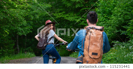 Travellers couple going on e-bike ride in nature. Tourist riding electric bicycles on easy trail road in the middle of forest. Young tourist spending summer vacation oudoors. Travellers couple going on e-bike ride in nature. Tourist riding electric bicycles on easy trail road in the middle of forest. Young tourist spending summer vacation oudoors. 115231441
