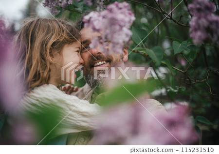 Dad embracing young daughter, carry her, looking at her lovingly, walking in spring nature. Fatherhood and Father's Day. 115231510