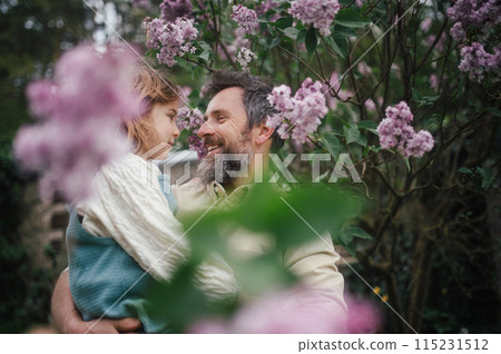 Dad embracing young daughter, carry her, looking at her lovingly, walking in spring nature. Fatherhood and Father's Day. Dad embracing young daughter, carry her, looking at her lovingly, walking in spring nature. Fatherhood and Father's Day. 115231512